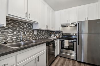 A kitchen with white cabinets and a black and white tiled backsplash.